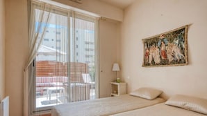 Une chambre d’hôtel avec deux lits, un tableau au mur, une fenêtre avec des rideaux et une vue sur le balcon extérieur.