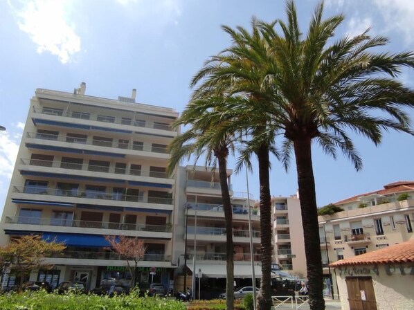 A multi-story building with balconies, a pharmacy, and parked cars.