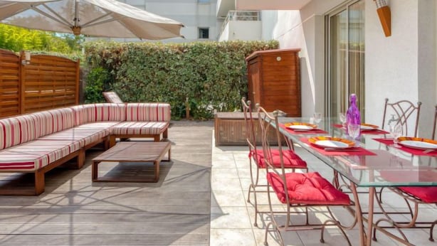 Une terrasse dotée d’une plateforme en bois, d’un canapé à rayures et d’une table en verre, le tout disposé pour les repas.