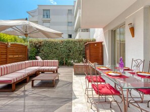 A patio with a wooden deck, a striped sofa, and a glass table set for dining.