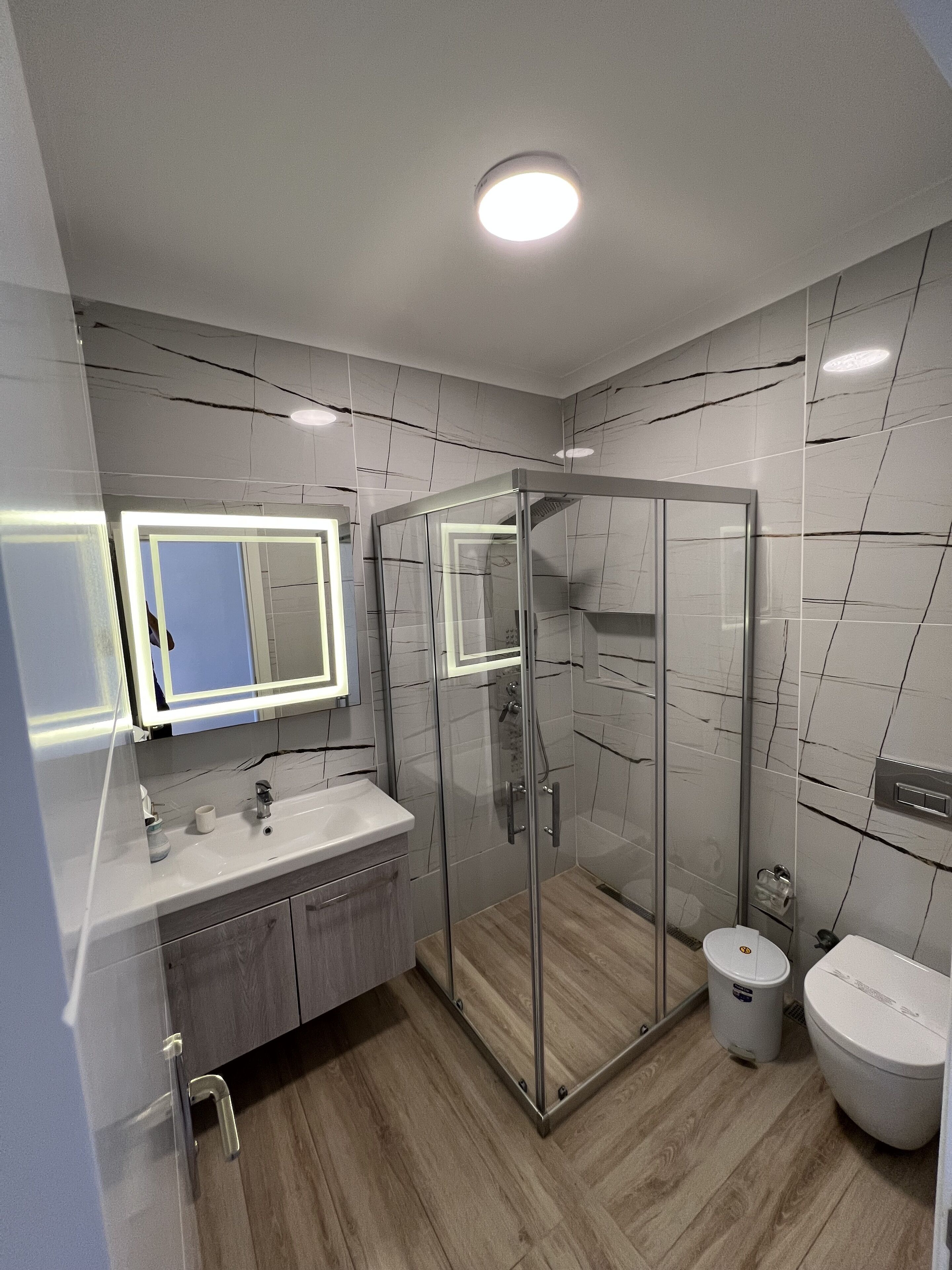 A modern bathroom with a glass-enclosed shower, a vanity with a mirror, and a toilet.