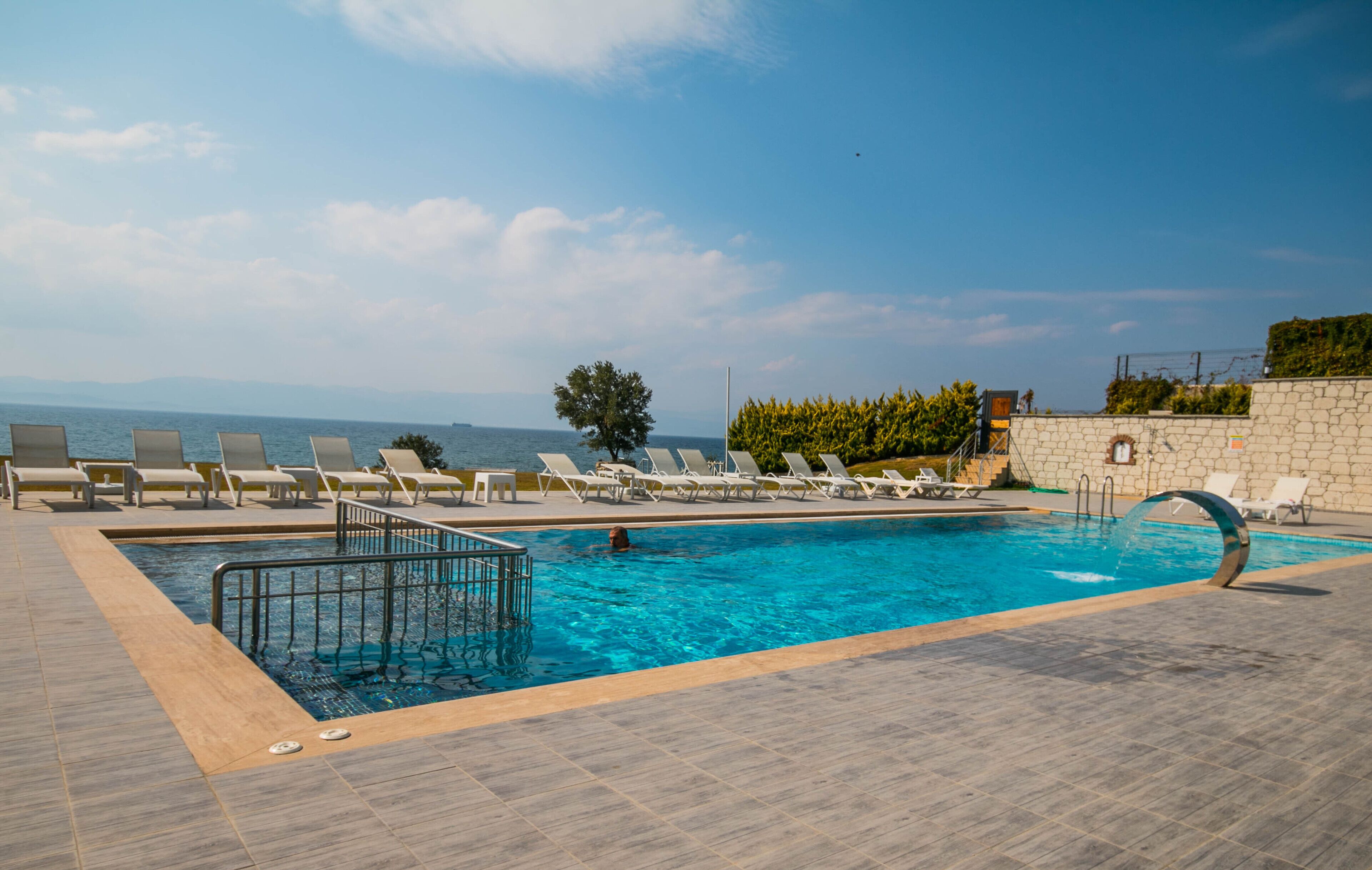 Una piscina con sillones de descanso y vista al mar.