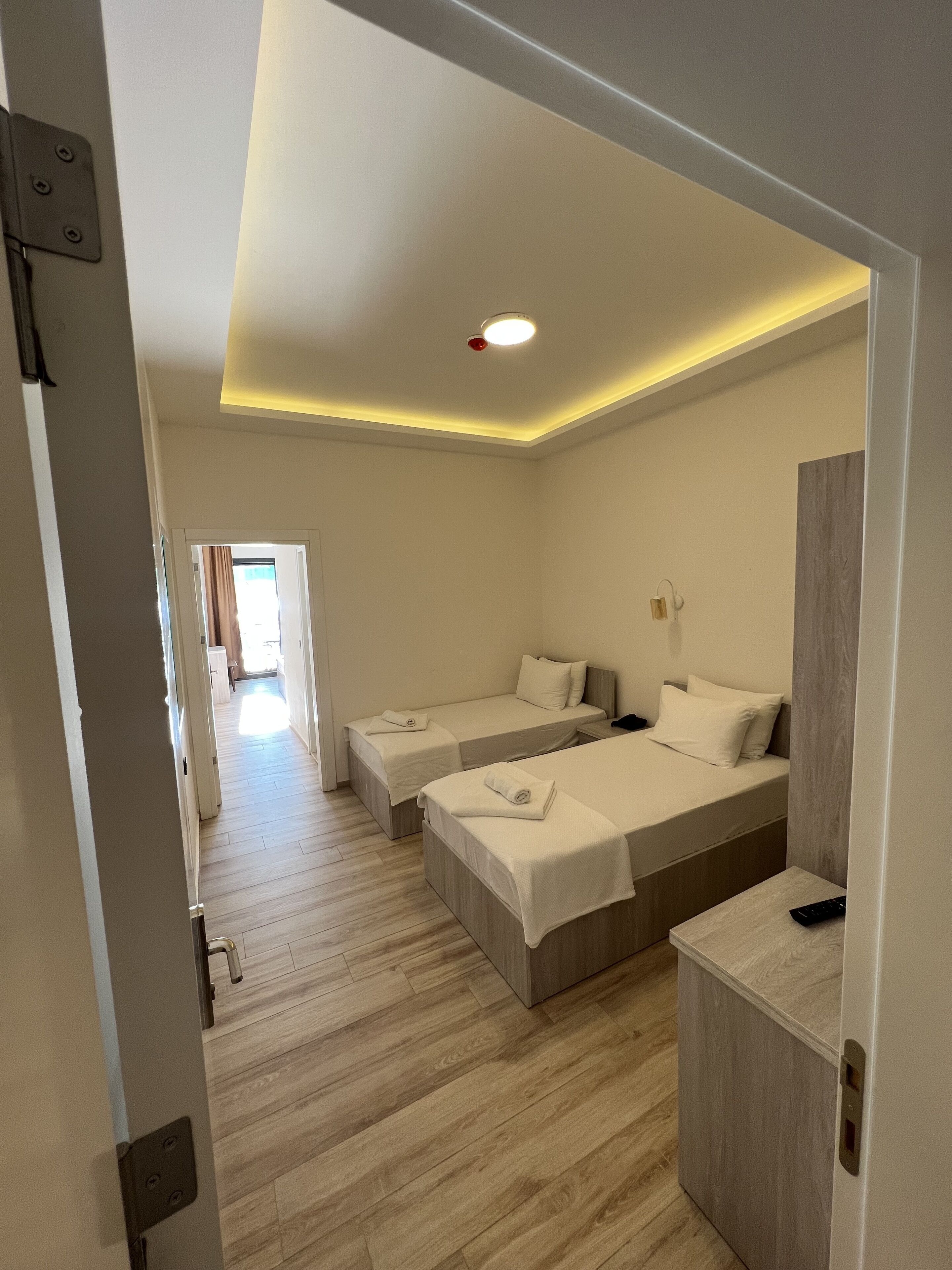 Habitación de hotel con dos camas individuales, suelo de madera, un escritorio pequeño con una silla y un espejo.