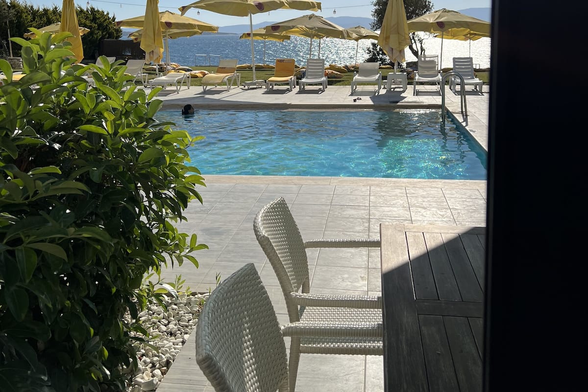 A poolside area with lounge chairs and umbrellas, a clear view of the sea, and a tiled deck.