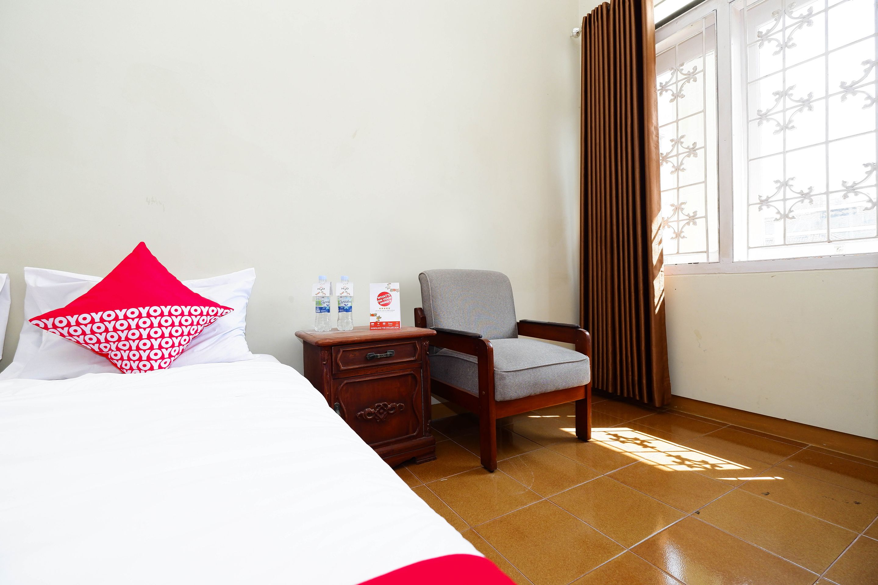 A hotel room with a bed, a nightstand, a chair, and a window with curtains.