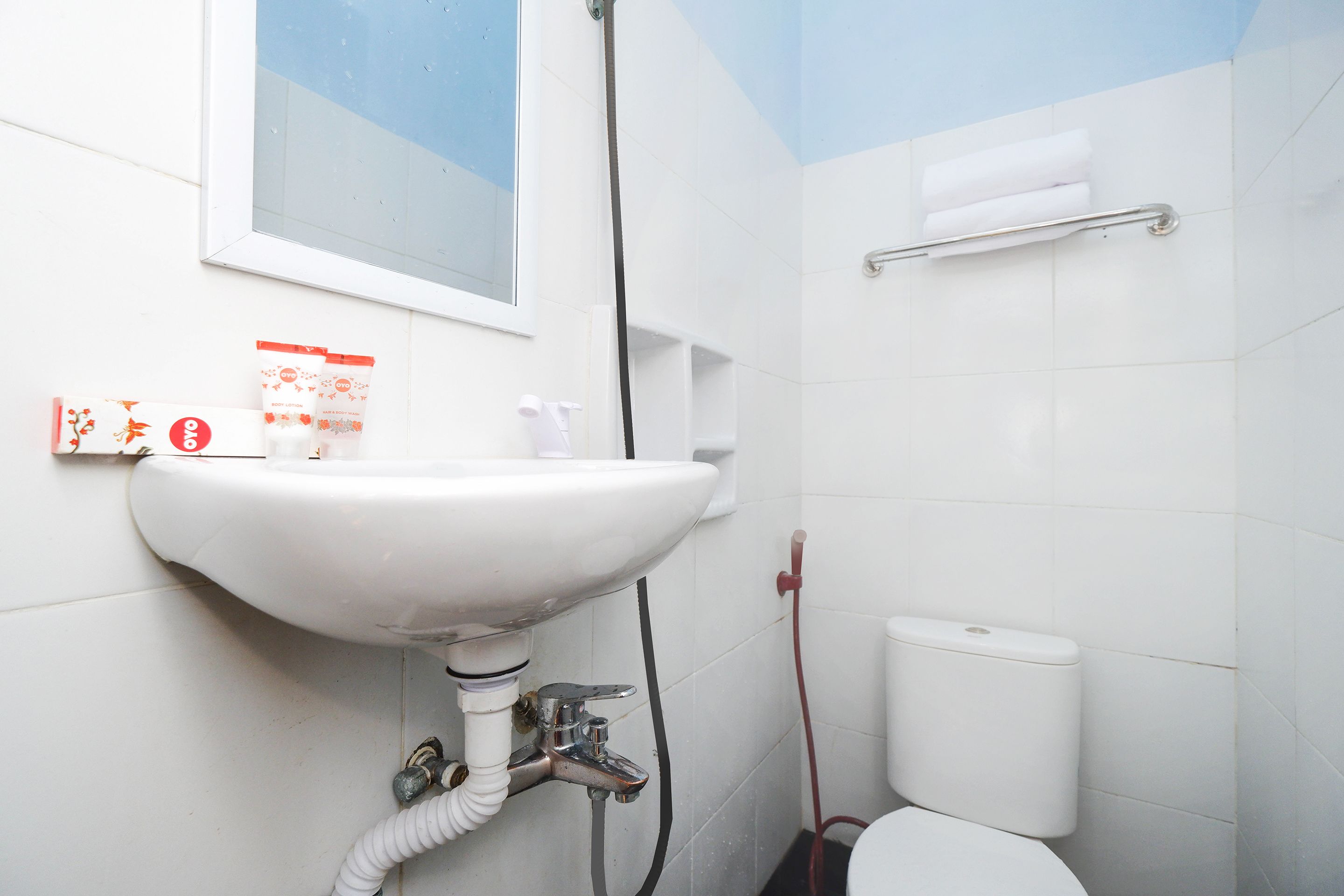 A bathroom with a white sink, toilet, and shower. There is a window above the sink and a towel rack on the wall.