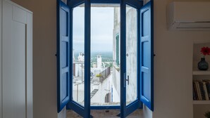 Una habitación con vistas a través de una ventana de marco azul, una puerta blanca y una estantería llena de libros.