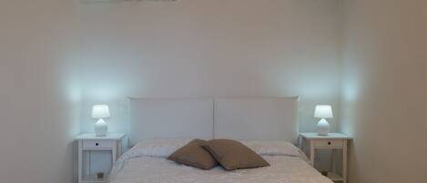 A bedroom with a stone ceiling, a bed with white bedding, two nightstands with lamps, and a small shelf on one nightstand.