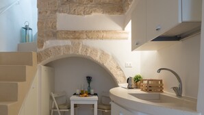 Una cocina estrecha con un arco de piedra, un lavamanos y una pequeña mesa con una silla.