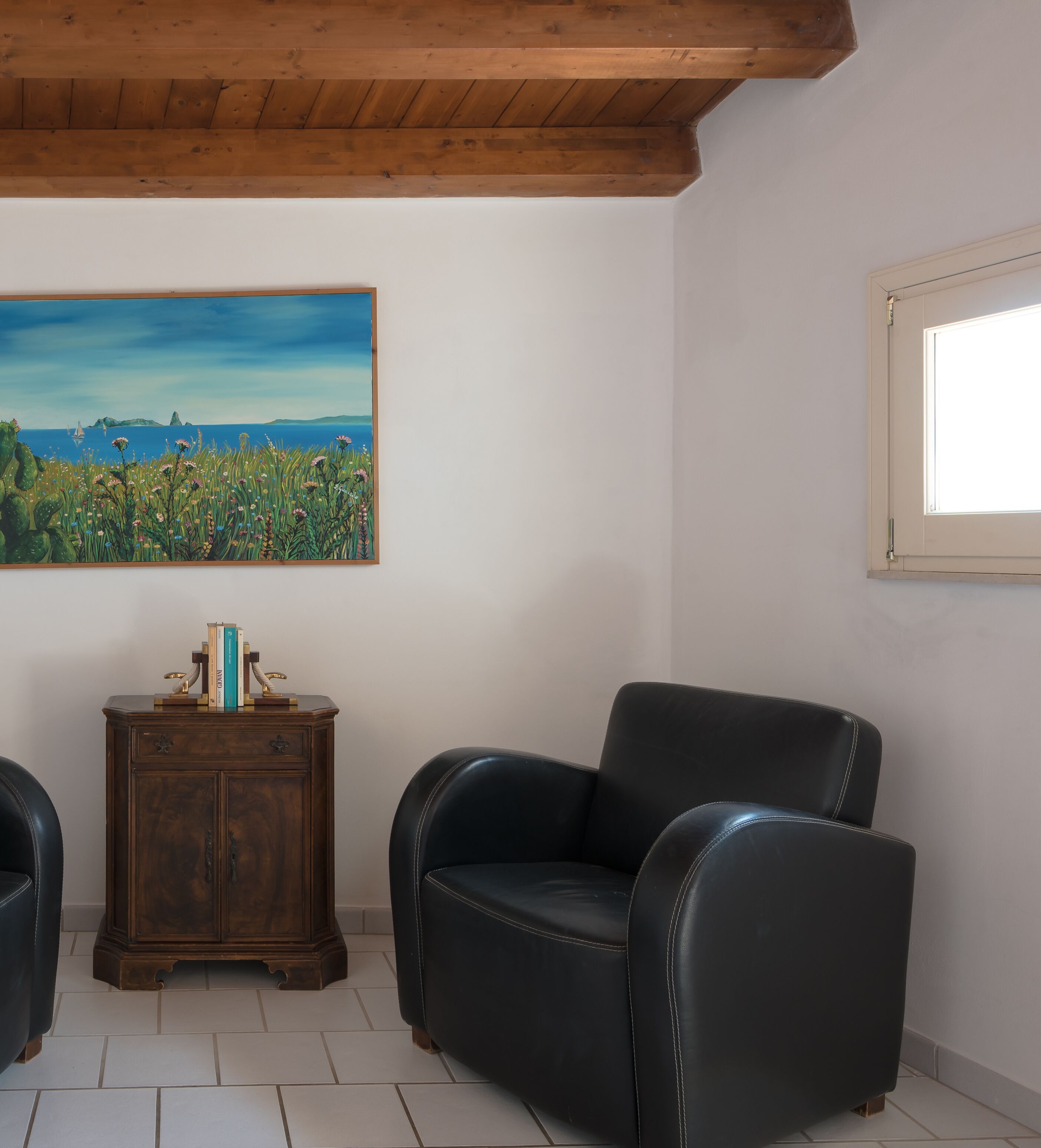 Una habitación con techo de madera, un cuadro de un paisaje, un sillón de cuero negro, un mueble de madera y una ventana.