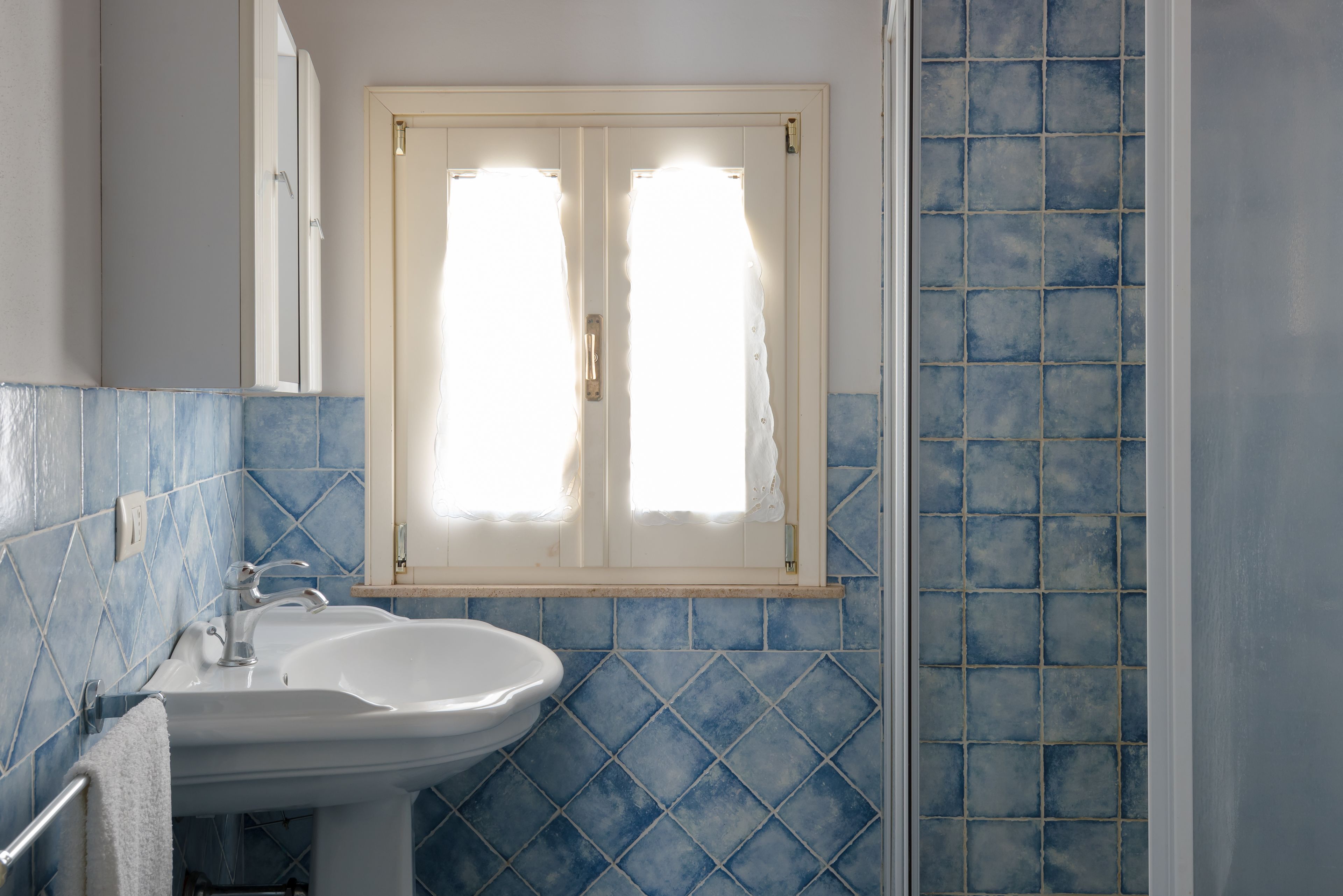 A bathroom with a white sink, blue tiles, and a window with curtains.