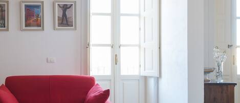 A red sofa in a room with a checkered floor, white walls, and wooden beams on the ceiling.