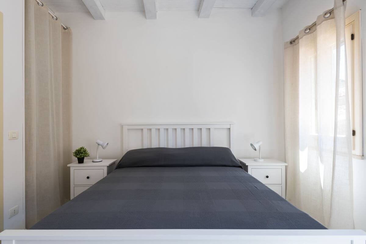 Une chambre à coucher avec un lit, deux tables de chevet, une commode, une lampe et une petite plante.
