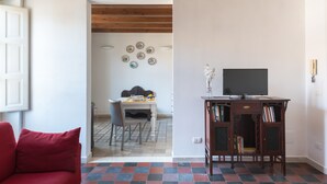 Ein Wohnzimmer mit einem roten Sofa, einem Fernseher auf einem Holzboden und einem Essbereich mit Tisch und Stühlen.