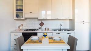 Eine moderne Küche mit weißen Schränken, einem Gaskochfeld und einer Spüle. Ein Esstisch mit Stühlen und eine Schüssel Zitronen darauf.