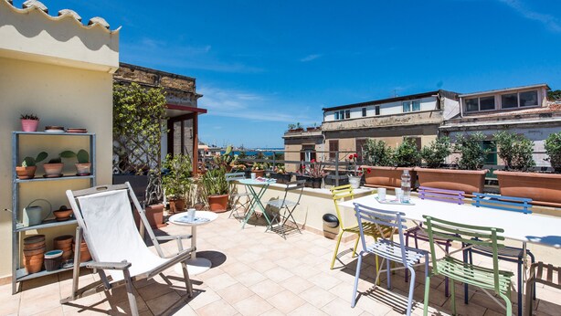 A rooftop patio with a table and chairs, surrounded by potted plants and a view of the city. - Terrazza dei Colori alla Kalsa by Wonderful Italy (Palermo)