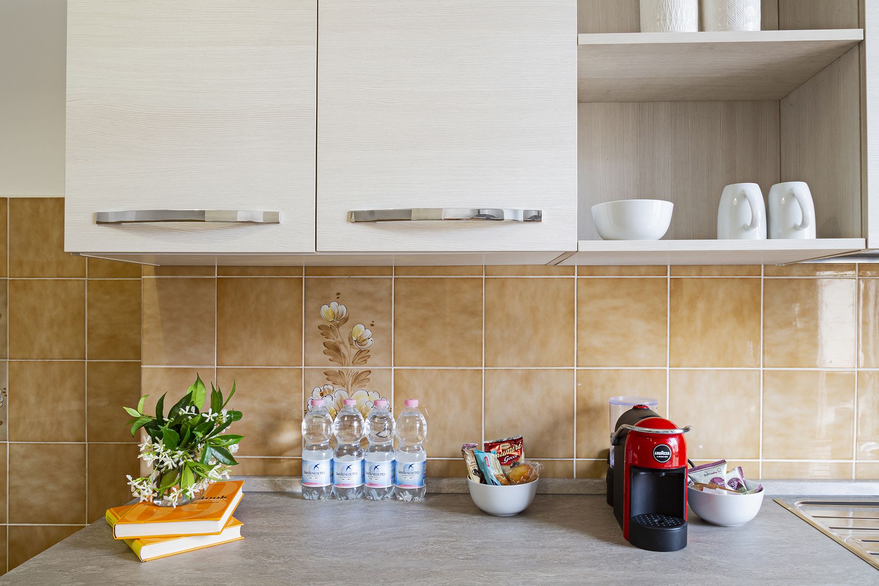 Una cocina con armarios de madera clara, salpicadero de azulejos y una cafetera.