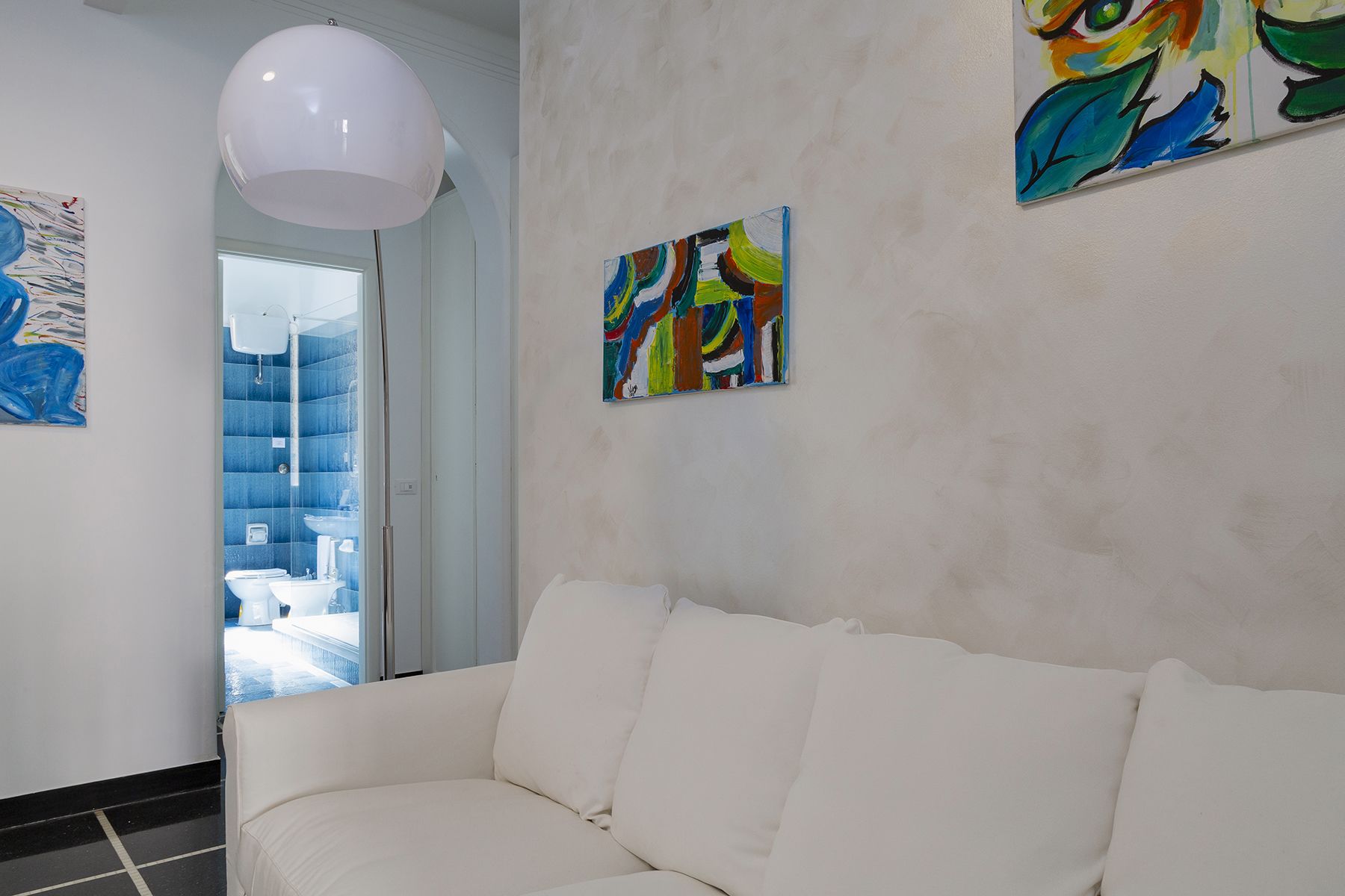 A modern interior with a white sofa, abstract paintings, and a large white pendant light.