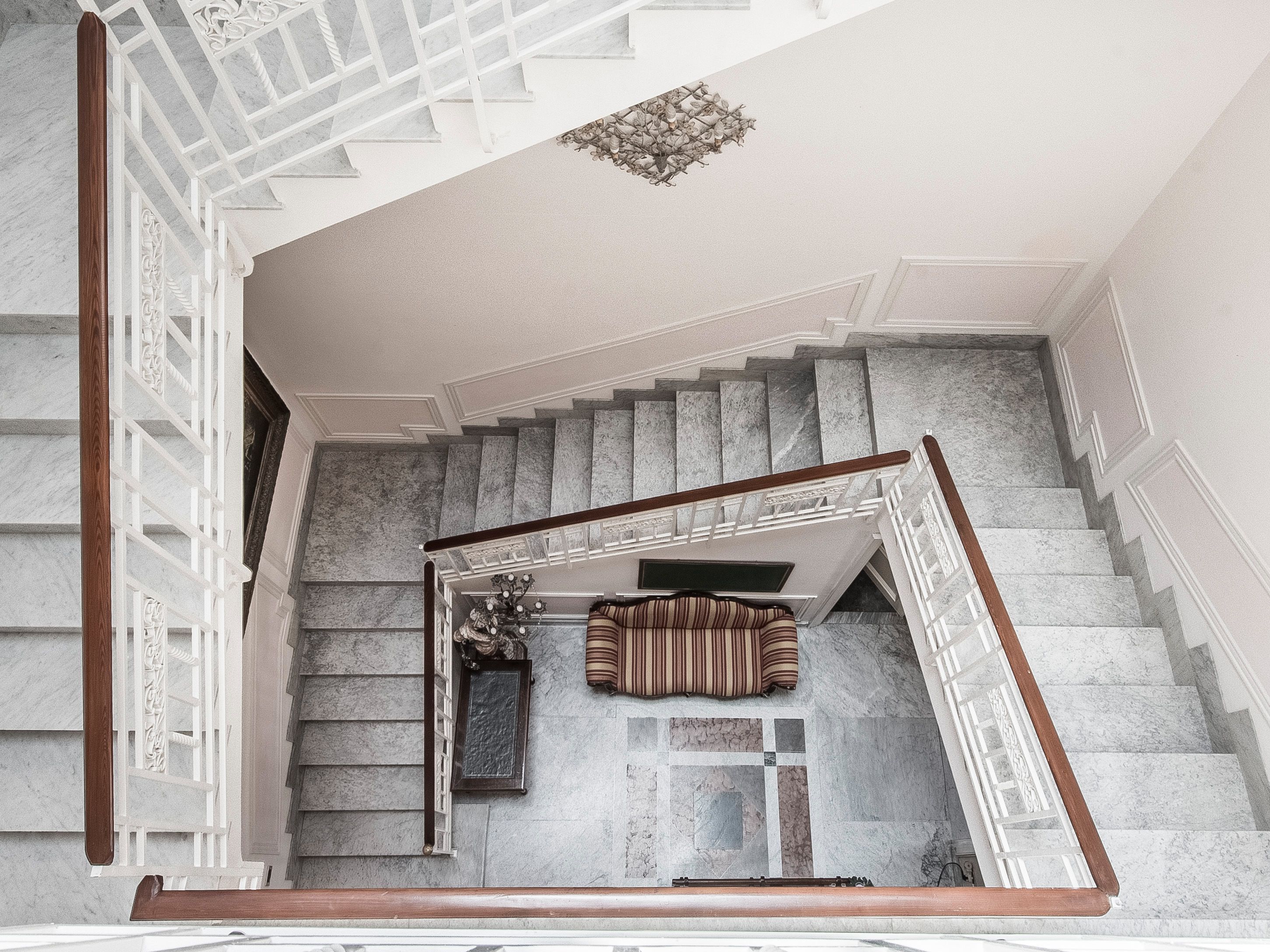 Una maestosa scalinata con gradini in marmo e una ringhiera in legno, che conduce a un pianerottolo con un tappeto decorato e un quadro incorniciato.