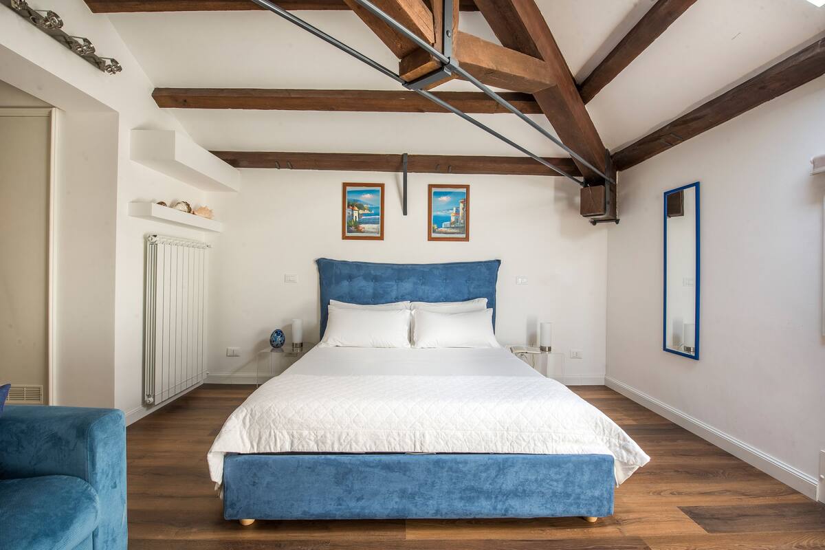 Een slaapkamer met een groot bed, houten balken, witte muren en twee ingelijste foto's aan de muur.
