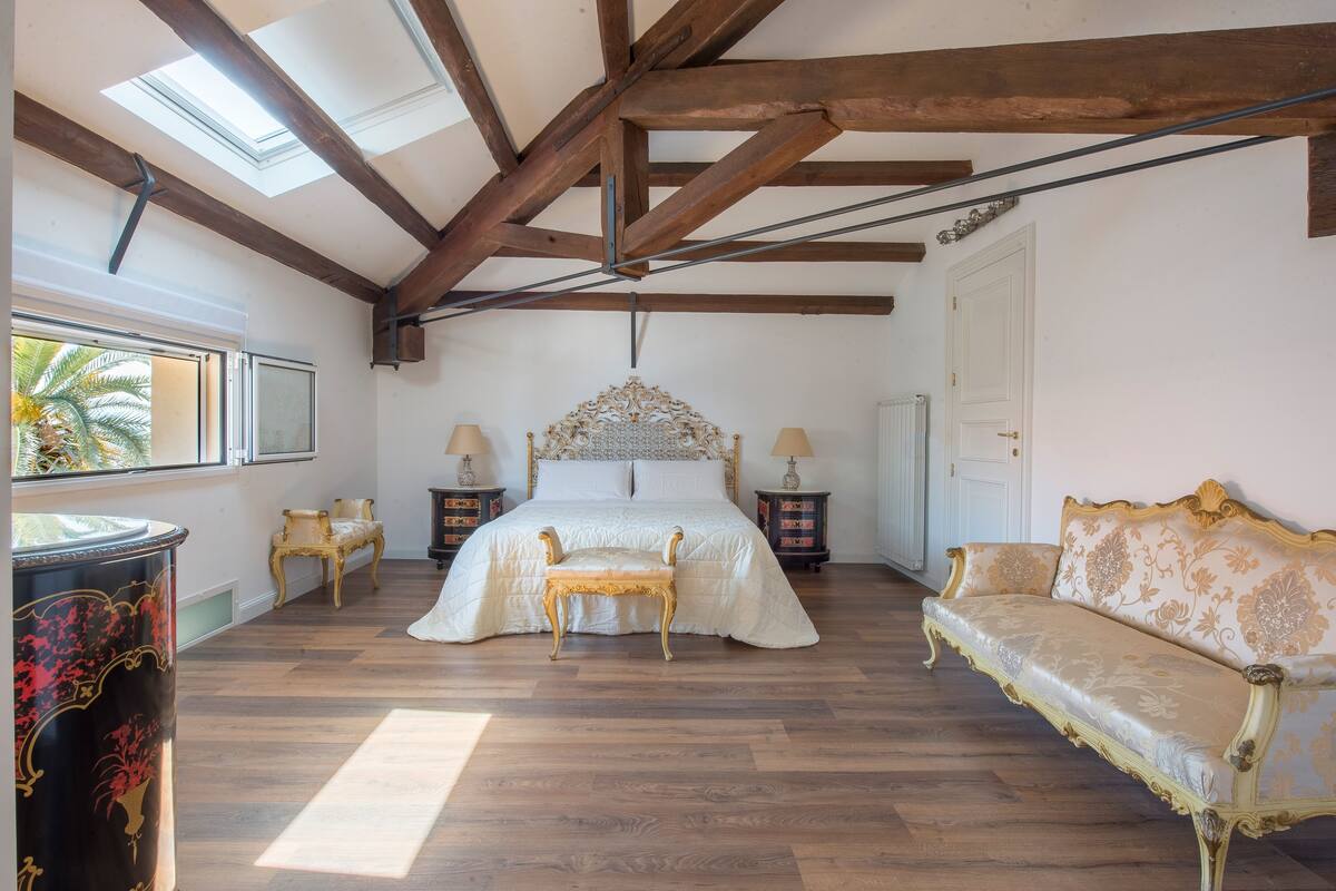 Een slaapkamer met een groot bed, een slaapbank, een stoel en een nachtkastje met lampen.