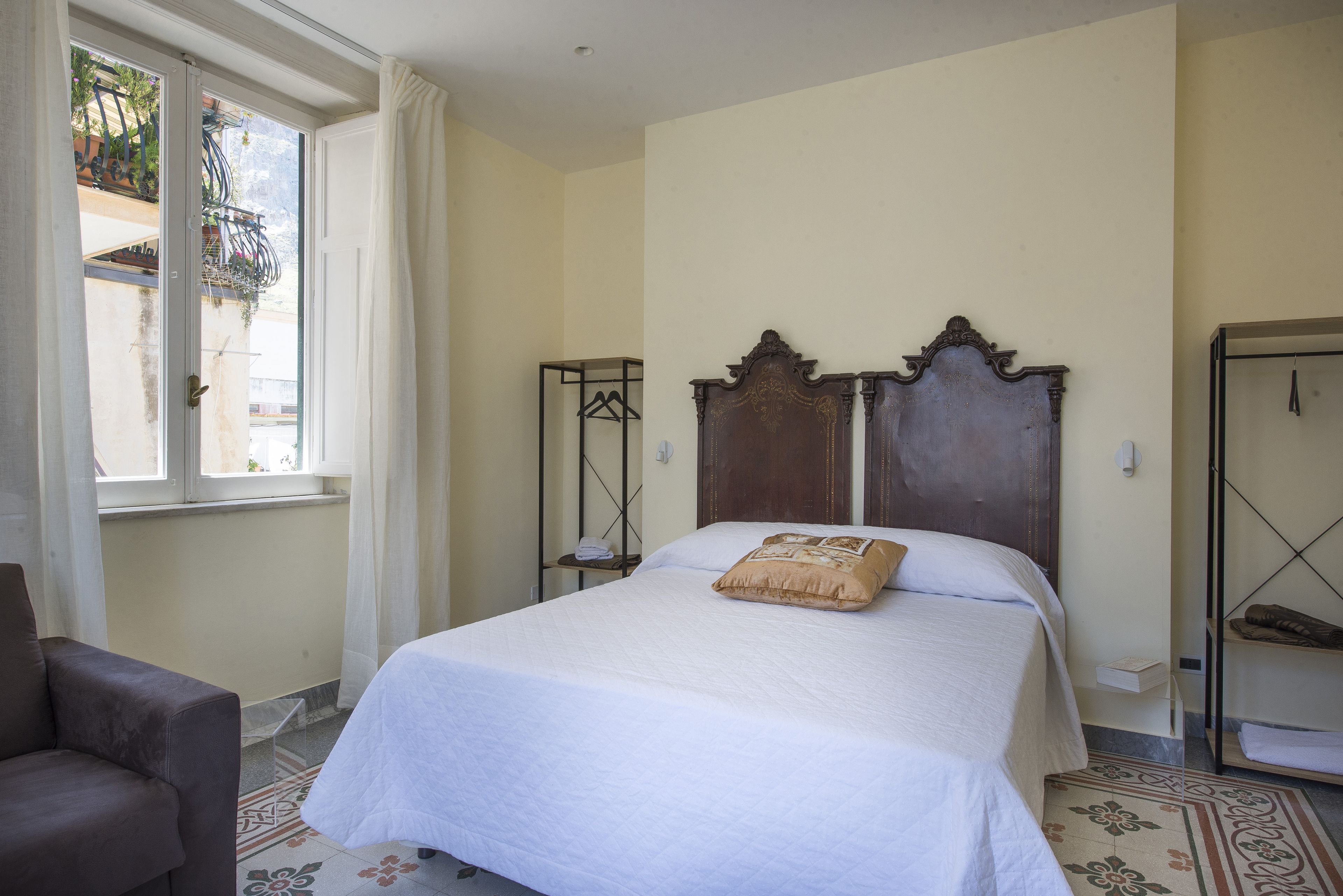 Un dormitorio con cama, una silla, ventana y balcón.