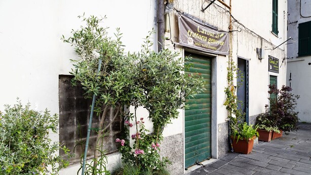 A narrow street with a building featuring a green door and a sign that reads "Lavour 21 trattoria genovese".