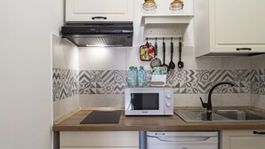 A compact kitchen with a microwave, sink, and dishwasher. There are two jars on the wall above the sink and a fruit basket on the countertop.