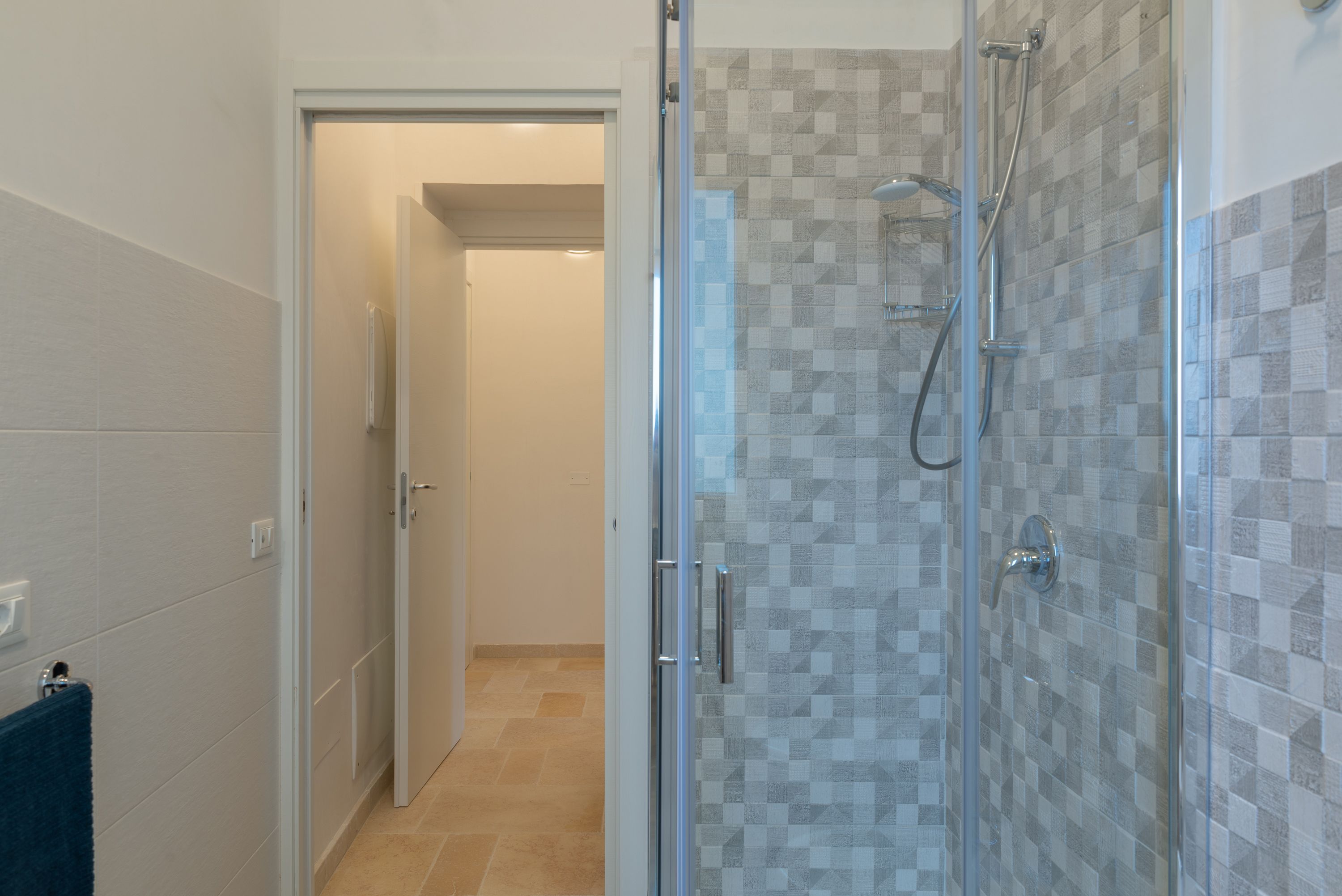 Un baño con cabina de ducha de vidrio, paredes con azulejos y un perchero visible.