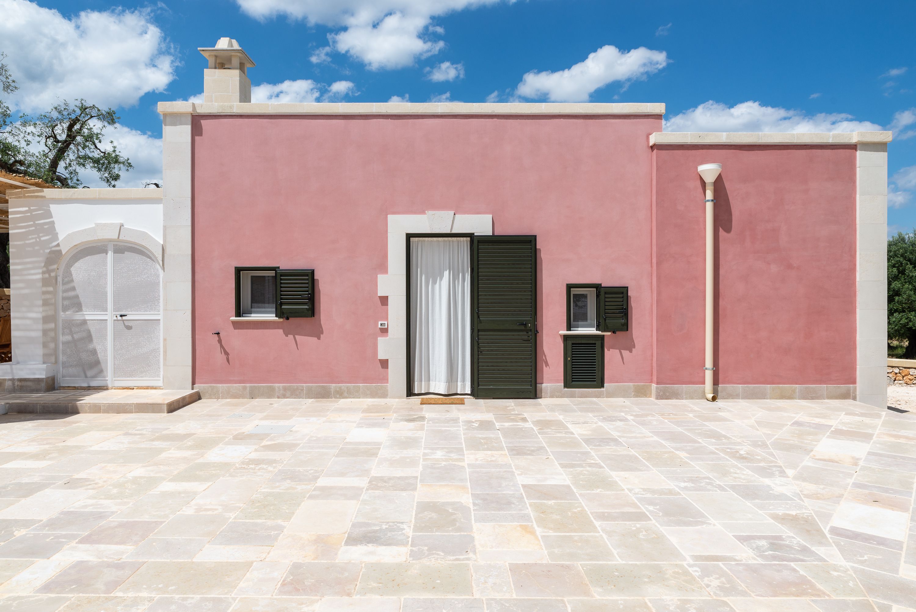 Un bâtiment à la façade rose, doté d’un patio carrelé et d’une porte blanche avec des volets.