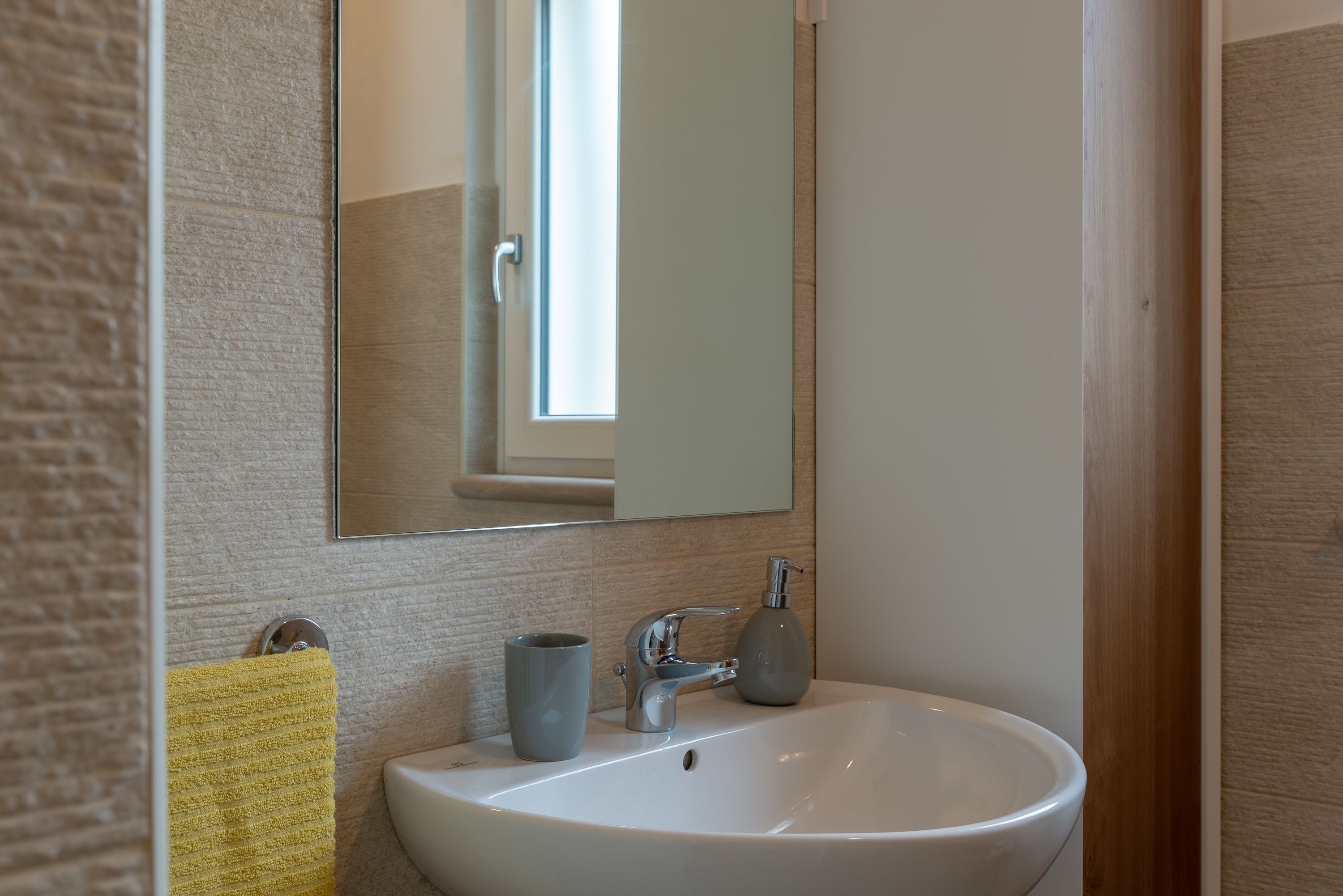 A bathroom with a white sink, a mirror, and a yellow towel hanging on a towel rack.