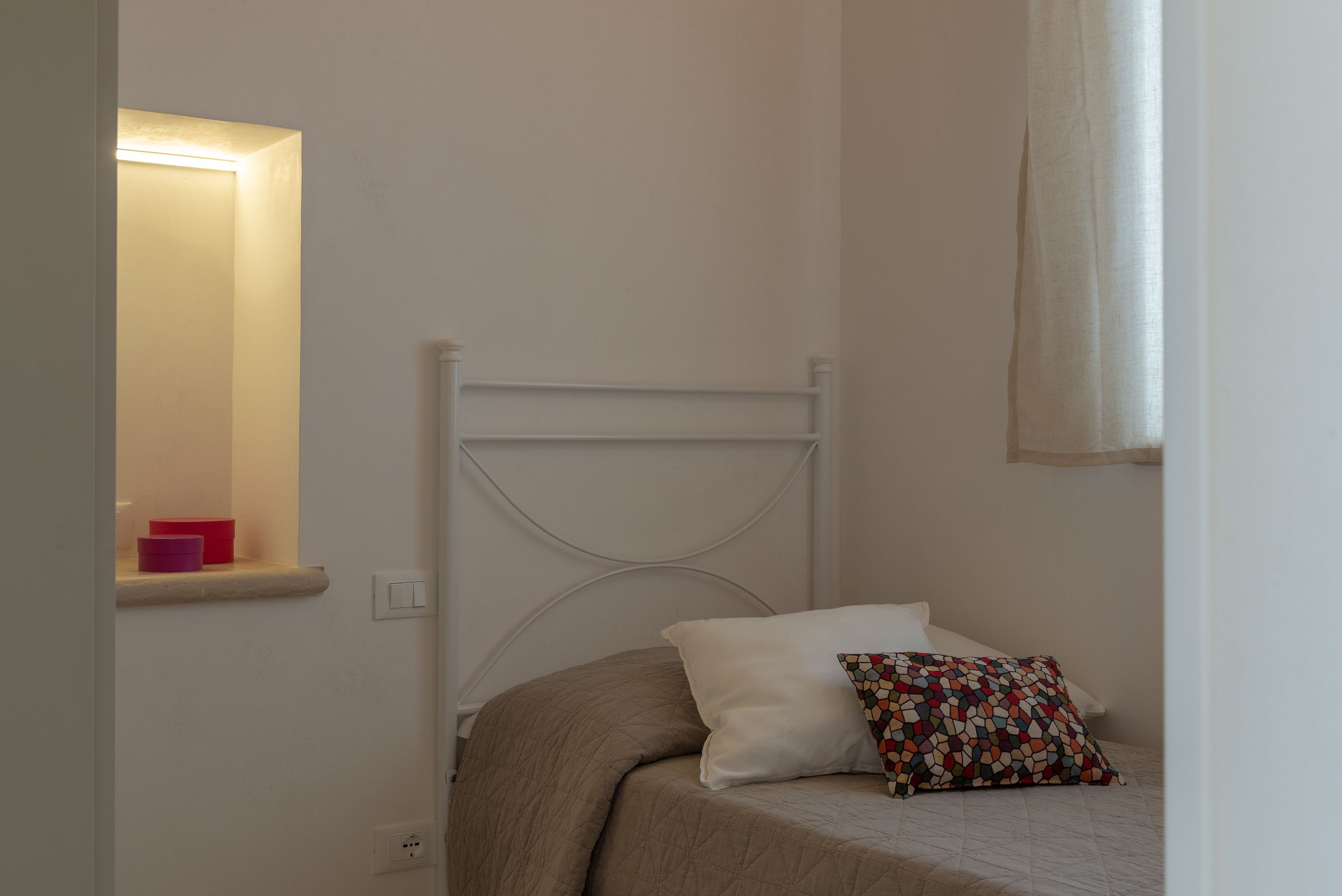 Una camera da letto con un letto, un comodino e una finestra con tenda.