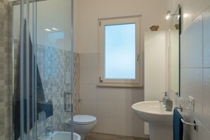 Een badkamer met een douchecabine van glas, een toilet, een wastafel en een raam.