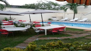 An outdoor patio area with tables and chairs, a pool, and a palm tree. - Residence Divine Palace (Abidjan)