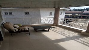 A balcony with a sofa and a table, a tiled floor, and a view of buildings in the background. - Residence Divine Palace (Abidjan)