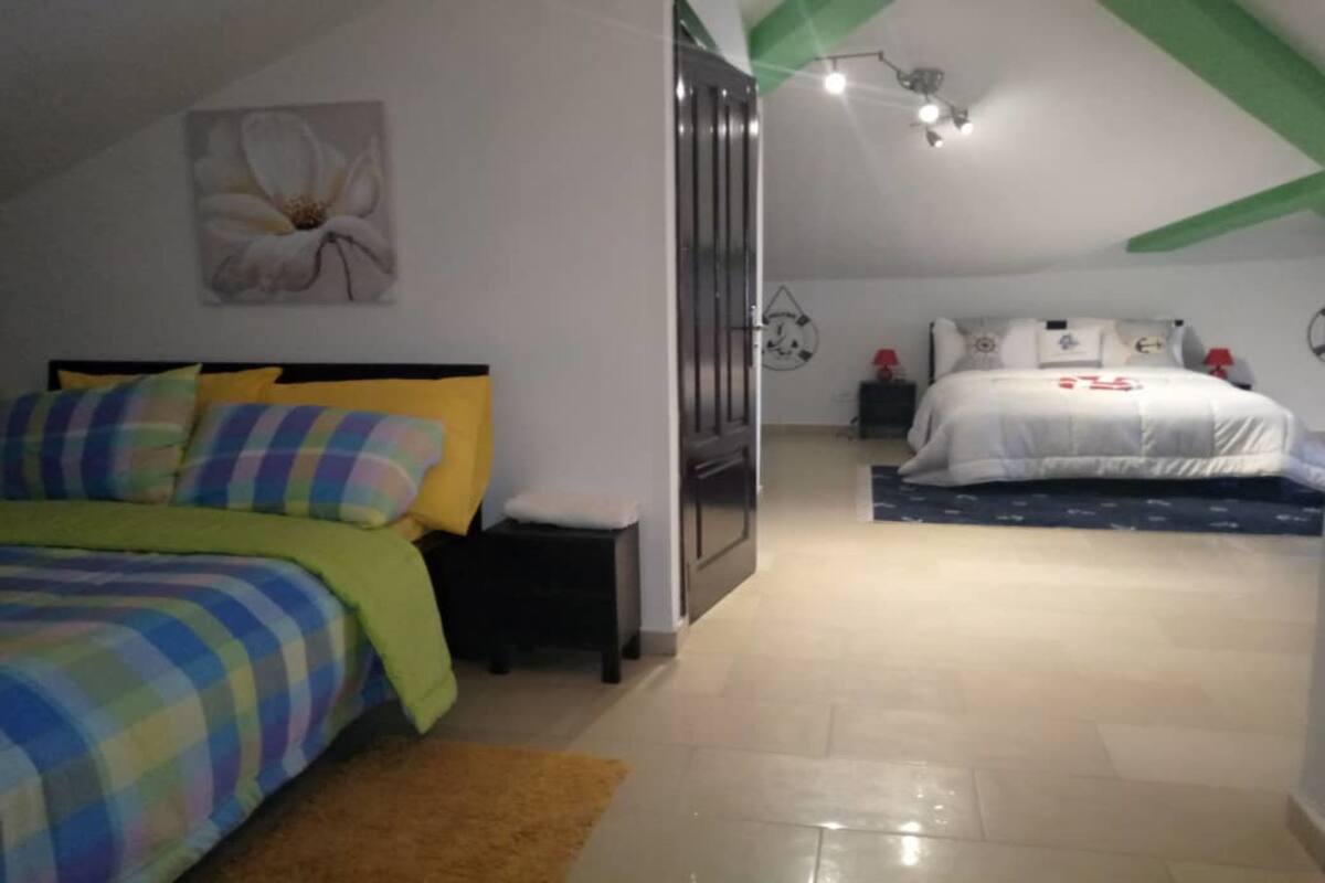 A bedroom with a bed, a nightstand, a small table, and a wall-mounted shelf.