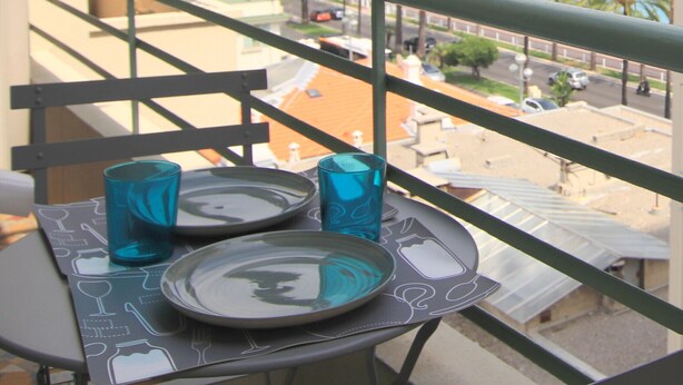 A balcony with a table set for two, overlooking a coastal view.
