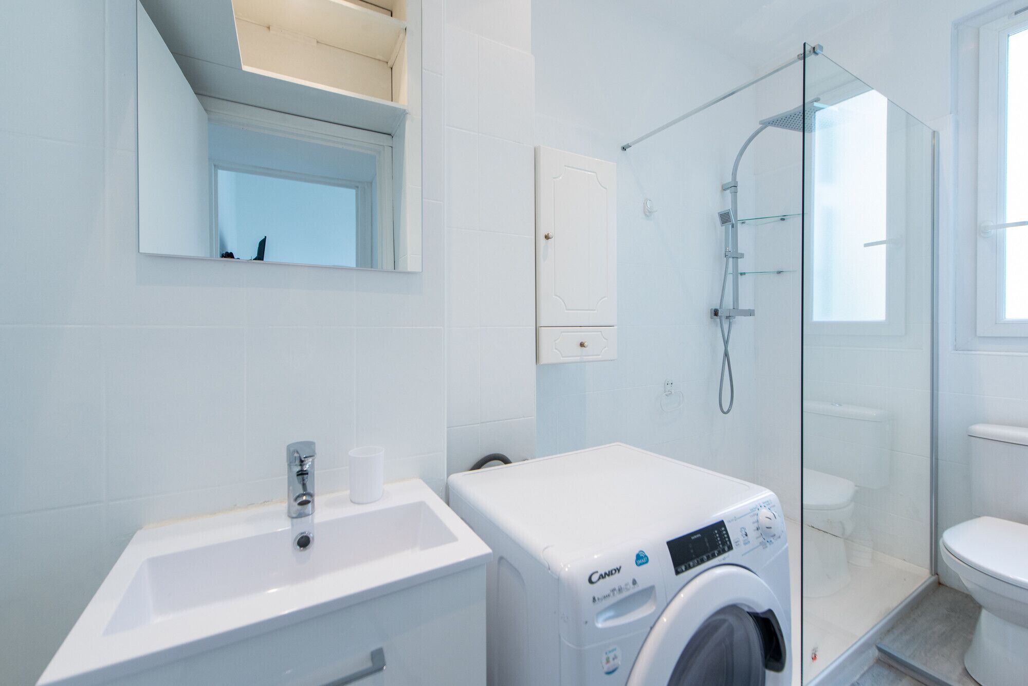 A modern bathroom with a sink, mirror, toilet, shower, and a washing machine.
