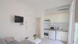 A compact living space with a sofa, a small table, a TV, a kitchenette with a microwave, and cabinets.