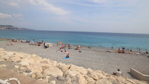 A beach with people sunbathing and swimming, rocky terrain, and a clear sky.