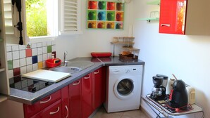 Kompakti keittiö, jossa on punaiset kaapit, pesukone, kahvinkeitin ja ikkuna, jossa on sälekaihtimet.