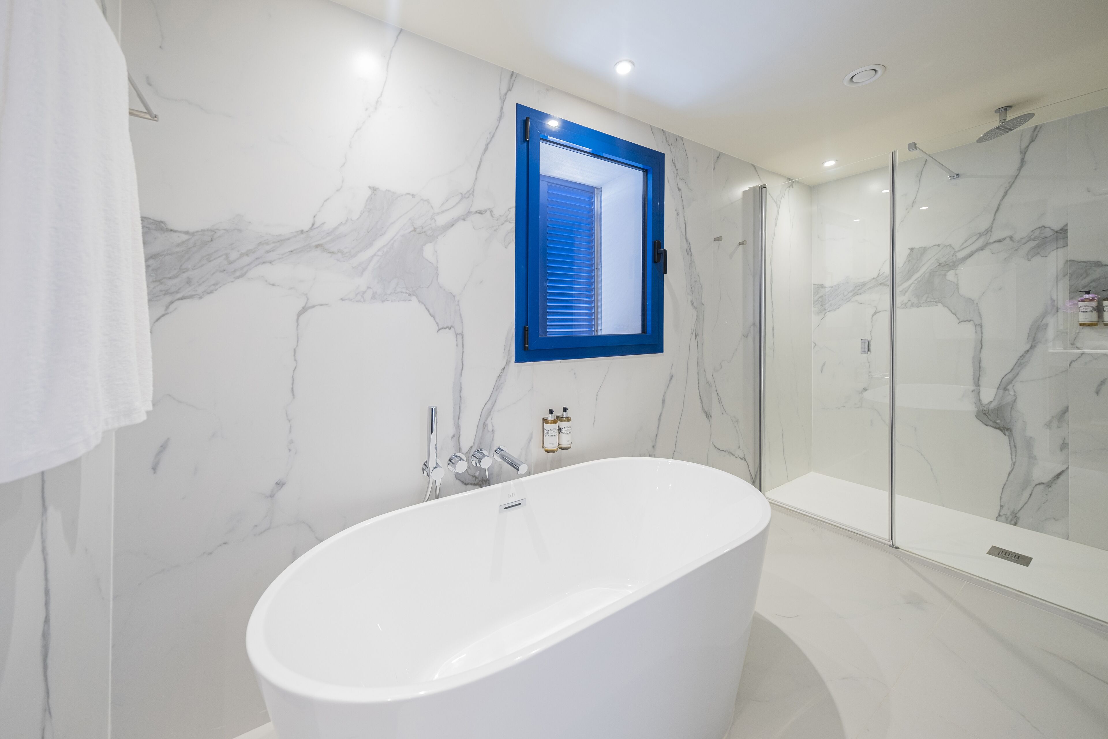 A modern bathroom with a freestanding bathtub, a glass shower enclosure, and marble walls.
