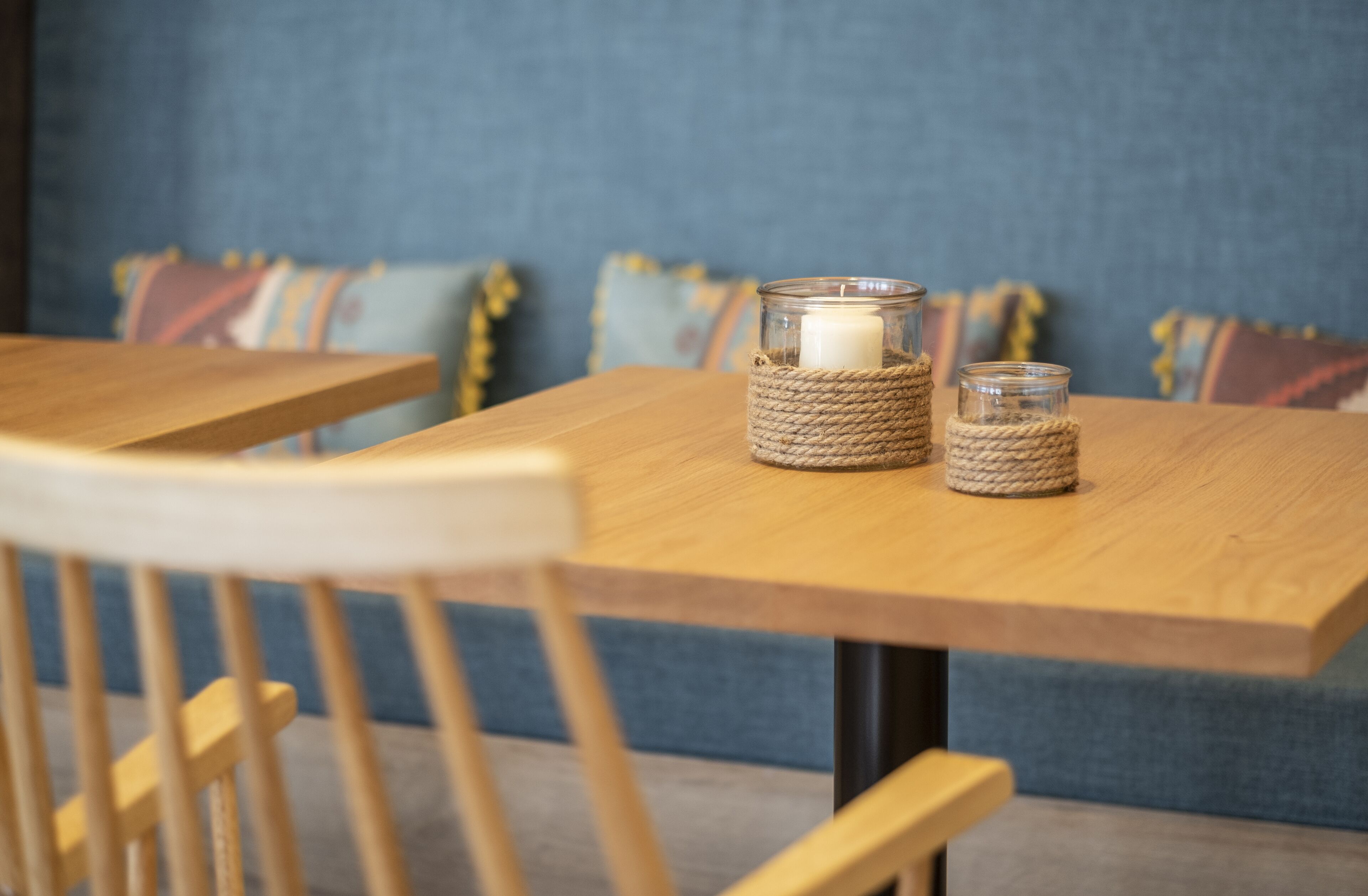 Een houten tafel met twee kandelaars van glas, waarvan één een basis van touw heeft en de ander een heldere glazen basis.