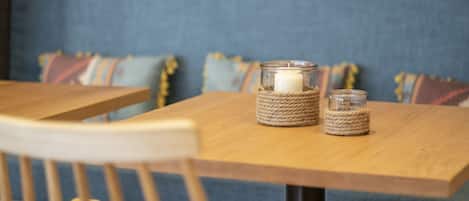 Une table en bois sur laquelle reposent deux chandeliers en verre : l’un a une base recouverte de corde, l’autre a une base en verre transparent.