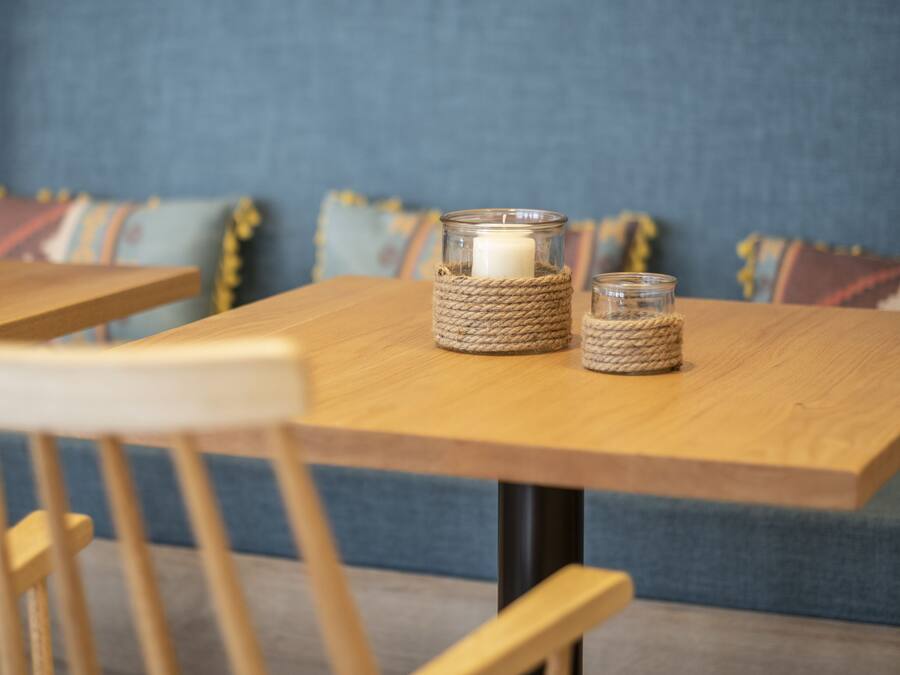 Een houten tafel met twee kandelaars van glas, waarvan één een basis van touw heeft en de ander een heldere glazen basis.