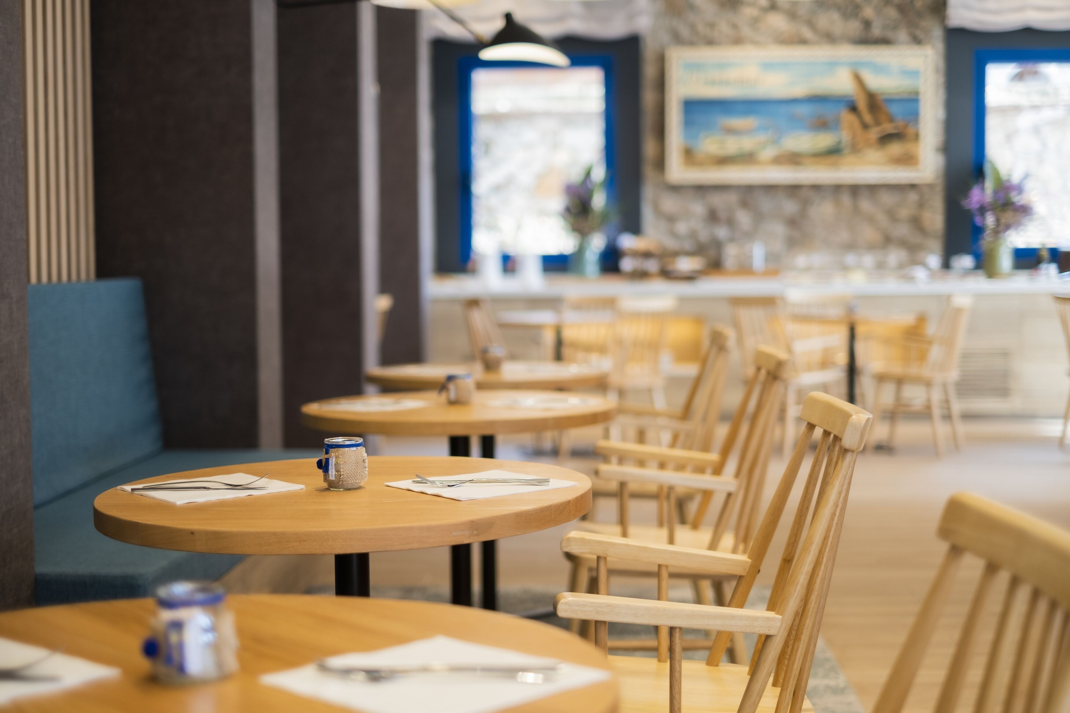 A restaurant with round wooden tables and chairs, a stone wall, and a painting on the wall.