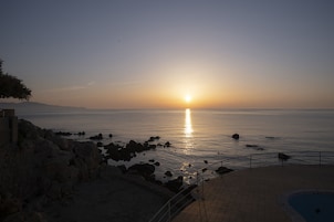 Vista al atardecer desde un balcón con vista a una playa rocosa y una piscina.