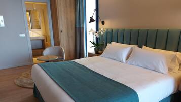 A modern hotel room with a large bed, a small round table, a chair, and a view of the outside.