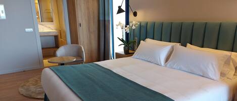 A modern hotel room with a large bed, a small round table, a chair, and a view of the outside.
