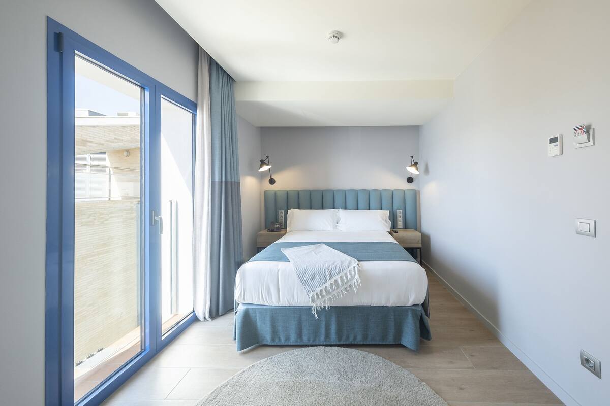 A bedroom with a large sliding glass door, a bed with a blue headboard, and two bedside lamps.